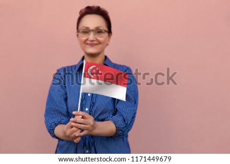 Singapore flag. Woman holding Singapore flag. Nice portrait of middle aged lady 40 50 years old with a national flag over pink wall background outdoors.