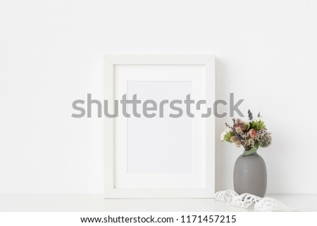 White a5 portrait frame mockup with dried field wild flowers in vase and vintage lace on white wall background. Empty frame, poster mock up for presentation design. Template frame for text, lettering