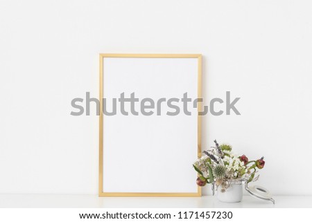 Gold a4 portrait frame mockup with dried field wild flowers in small white poton white wall background. Empty frame, poster mock up for presentation design. Template frame for text, lettering, modern