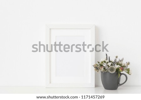 Molern white a5 portrait frame mockup with dried field wild flowers in mug on white wall background. Empty frame, poster mock up for presentation design. Template frame for text, lettering, modern art