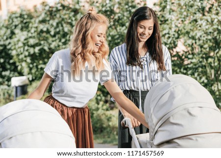 happy mothers looking at baby carriages in park