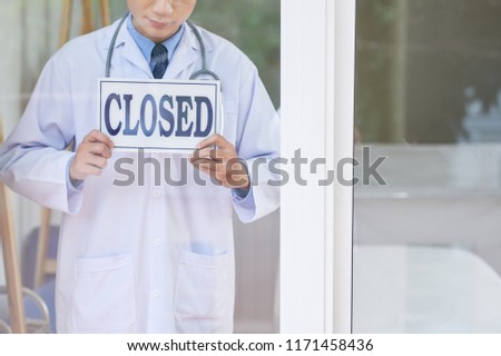 Anonymous guy in medical uniform holding sign with closed writing while standing behind glass in office