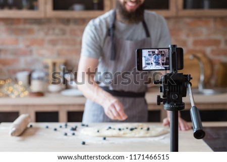 vlogging and freelance job concept. food blogger preparing blueberry pie. cooking and culinary skills concept. bearded man shooting video of himself using camera on tripod. Royalty-Free Stock Photo #1171466515