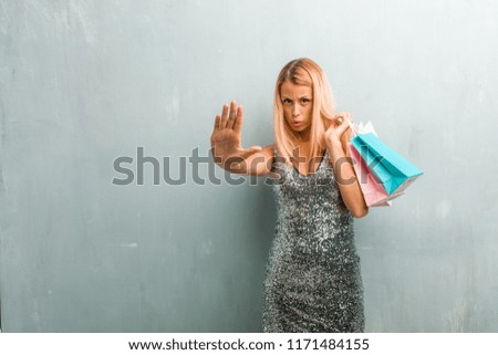Portrait of young elegant blonde woman serious and determined, putting hand in front, stop gesture, deny concept. Holding shopping bag.