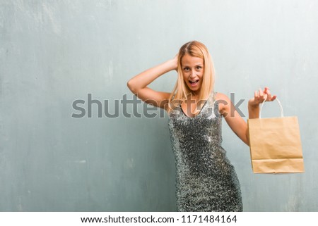 Portrait of young elegant blonde woman surprised and shocked, looking with wide eyes, excited by an offer or by a new job, win concept. Holding shopping bag.