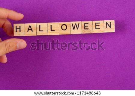A man's hand holds a wooden square with an inscription halloween on a purple background