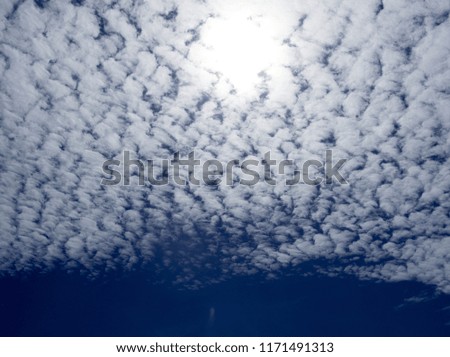 White fluffy clouds in the bright blue sky with glare and bright light of Sun