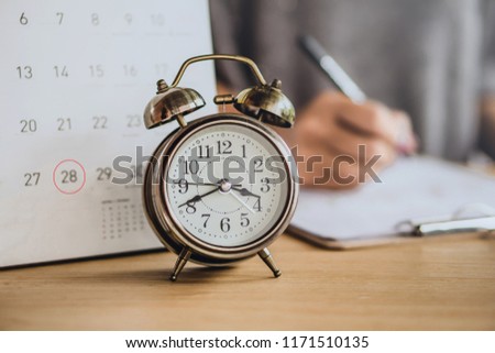 due date calendar with alarm clock on office desk and blur business woman working in background  Royalty-Free Stock Photo #1171510135