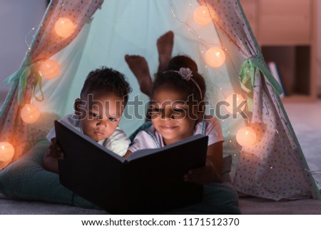 Little African-American children reading bedtime story in hovel Royalty-Free Stock Photo #1171512370