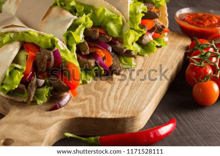 Wrap, Mexican food, fajitas, burrito, and tacos with salad, tomato, red onion and beef on wooden background. Fast food concept. 