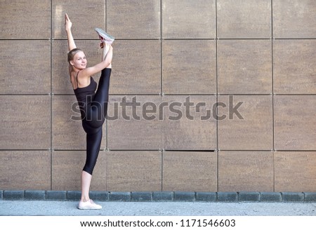 Stretching gymnast woman doing vertical split, twine in brown urban wall background.