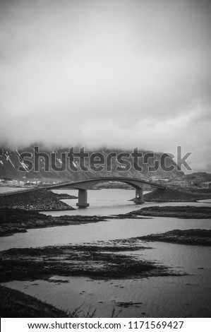 Landscape of Fredvang bridge across the island in Ramberg at Lofoten Norway.View of road with bridge over the sea with clouds, water and mountain in background-Image
