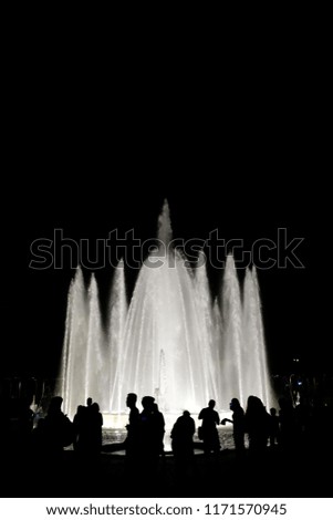Black and white photography. Silhouettes of people against the background of a fountain at night in the city