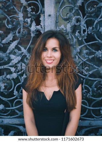 Portrait of brunette girl with long hair on vintage wrought iron gate background 