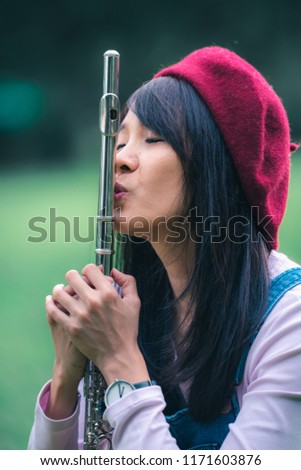 A beautiful woman posing in a park while playing on a flute.