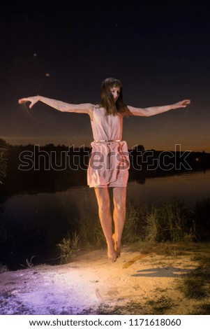 Girl in pink dress jumping on the river beach during sunset and white flour on the ground. Outdoor portrait. Unordinary photoshoot in night time