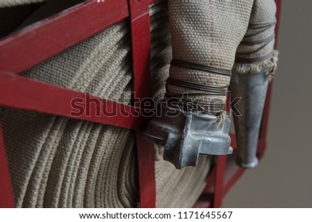 An old gray fire hose made of fireproof material attached to a special stand on a wooden wall. Connecting pipes made of metal.