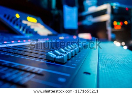 Low level view of a professional audio mixing console with rack equipment in the background