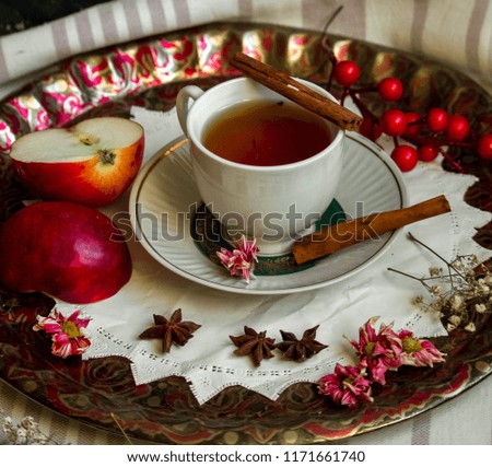 A cup of tea with red apples and cinnamon around on white