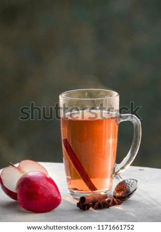 A cup of tea with red apples and cinnamon around on white