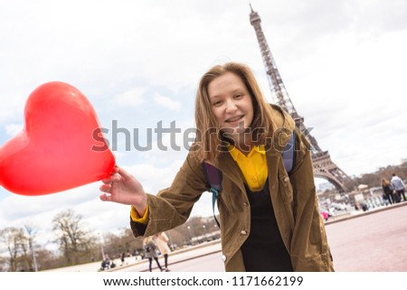 happy and smiling girl student with a balloon in the shape of a hearton the background of the Eiffel Tower in Paris. France 
