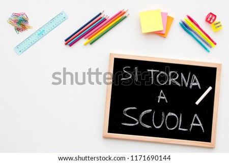 "Si torna a scuola" the italian translation of "Back to school" text on a blackboard. School desk with blank space, coloured paper clips, coloured pencils, ruler, pens
