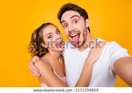 Self portrait of childish crazy couple shooting selfie on front camera gesturing tongue out having online meeting isolated on vivid yellow background