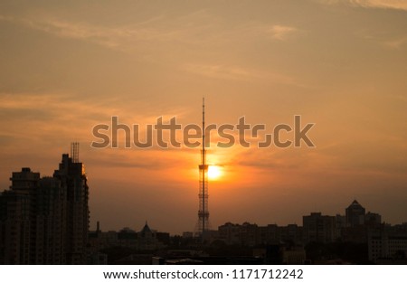 Bright sunset in the summer in the city. All the sky is yellow and orange and the dark television tower silhouette is at the centre of the picture. Colorful evening panorama. 