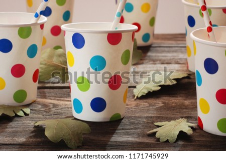 Paper cups in colored peas and autumn leaves on the background of wooden boards. Children's holiday.
