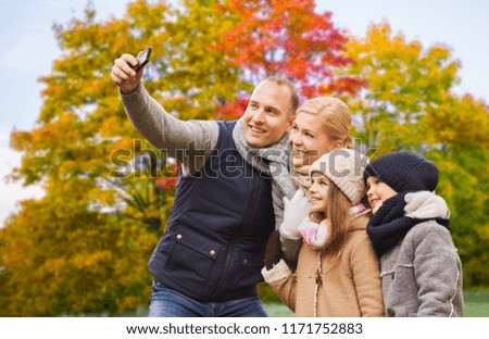 family, technology and people concept - happy mother, father, daughter and son taking selfie by smartphone over autumn park background