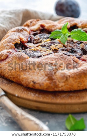 Pie with prunes, almond flakes and a sprig of mint on a wooden serving board, selective focus.