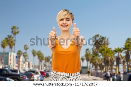 travel, tourism and summer holidays concept - happy smiling young woman showing thumbs up over venice beach background in california