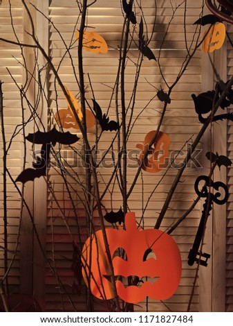 Halloween decorations made of paper. Jack o lanterns in orange color hanging on tree branches. Paper bats, cats and pumpkins as room decoration. Halloween traditional decor concept.