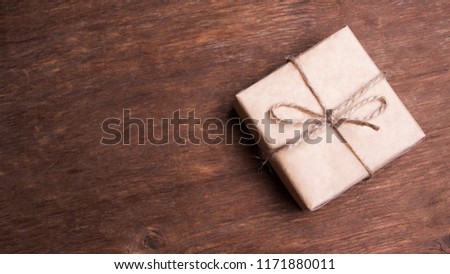 A gift in a kraft wrapper, tied with string on a wooden background. A natural present. Landing