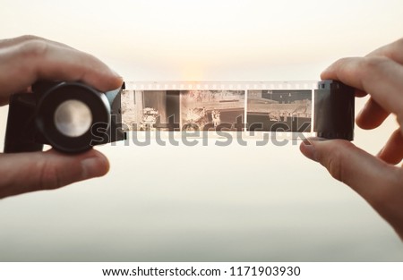 Male hands image using the Old vintage 35mm film Negative Viewer to see a frames on the sunset background Royalty-Free Stock Photo #1171903930