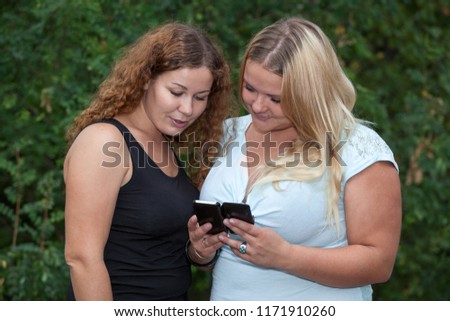 Two girl best friends discussing photos at smartphone screen, long blond and curly brunette