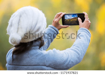 woman taking a picture of a beautiful forest in fall colors with her phone
