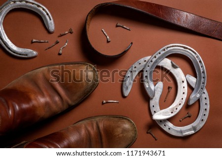 Horseshoes, nails, belt and a pair of leather shoes isolated on a brown background