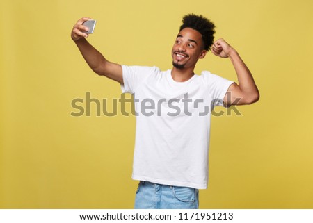 young afro american black man smiling happy taking selfie self portrait picture with mobile phone looking excited having fun posing cool isolated in yellow background in communication technology