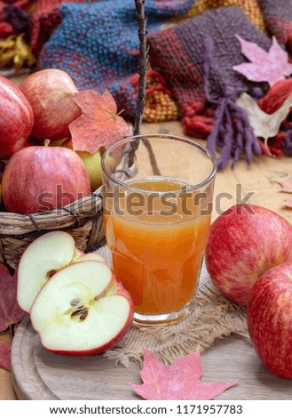 Glass of apple cider and fresh red apples with autumn leaves and colorful blanket in background