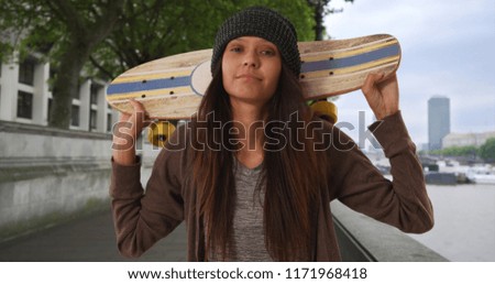Female Tourist with skateboard over her shoulders looking at camera in London