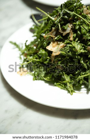 Close up on an arugula salad with balsamic vinaigrette dressing, garnished by parmesan cheese, on a marble table with space for text on bottom