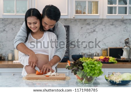 Attractive young husband embracing his pregnant wife while cooking vegetables food together in the kitchen. Concept healthy food, happy family. 