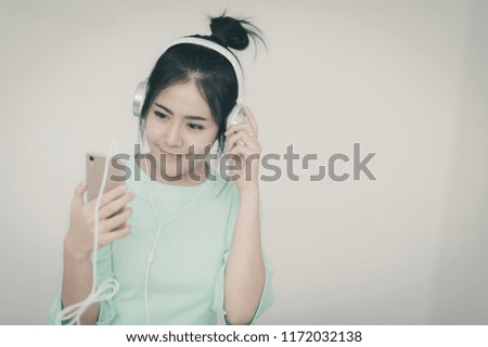 Young attractive Asian woman listening music on headphone while using smartphone for social network. Internet of things for modern lifestyle concept with vintage filter effect