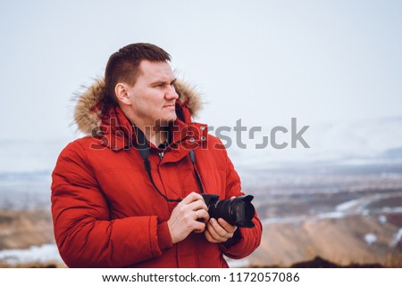 a serious man in a red down jacket with a camera travels to the mountains in winter
