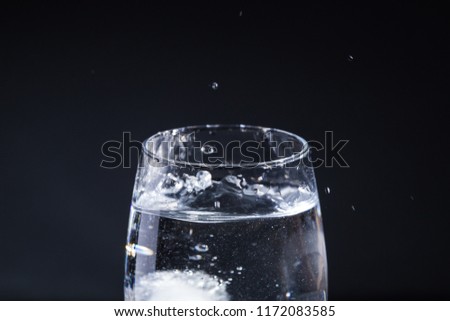 Glass of water on a gray background with drops in different directions
