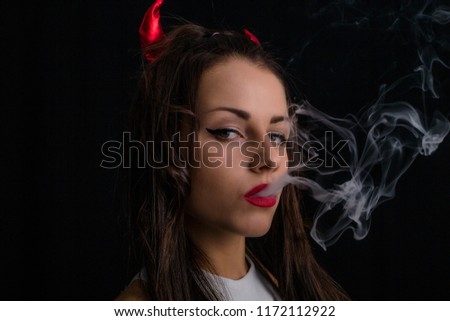 Woman with devil horns and cigarette smoke posing on black background