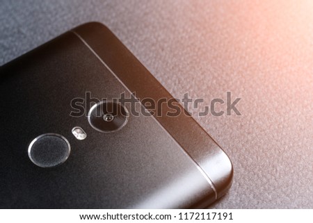 Black smartphone on a black textured surface is the back side. Toned glow.