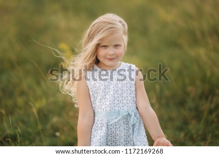 Little girl in sky blue dress stand in field in front of big tree
