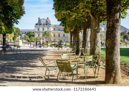 The Luxembourg garden in Paris, France, by a sunny summer morning with shady tree lined alley, people biking, strolling or resting on metal lawn chairs and the Luxembourg palace in the background.